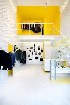 the inside of a clothing store with white walls and yellow accents