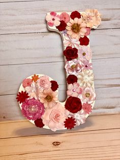 the letter j is made out of paper flowers and sits on a wooden table next to a wall