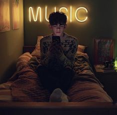 a person sitting on a bed with a cell phone in their hand and a neon sign above them