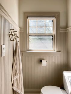 a white toilet sitting under a window next to a sink and towel rack in a bathroom