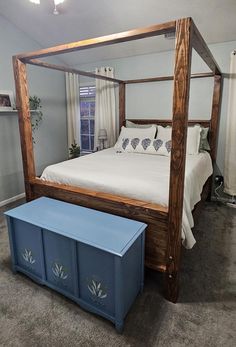 a bedroom with a canopy bed and blue chest under the foot board on the floor