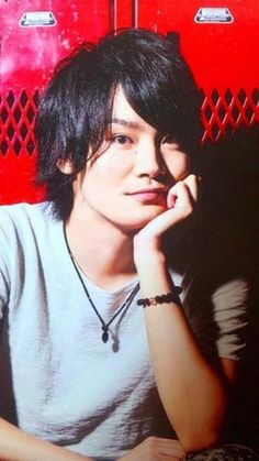 a young man sitting in front of a red wall with his hand on his chin