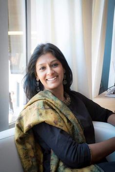 a woman sitting in front of a window with a scarf around her neck and smiling at the camera