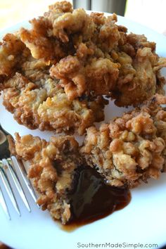 some fried food on a white plate with sauce next to a fork and spoons