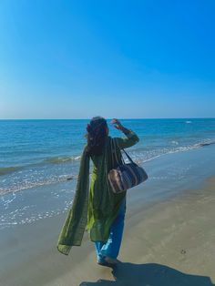 a woman is walking along the beach with her hand in her hair and wearing a green shawl