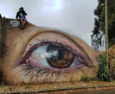 a man sitting on top of a wall with an eye painted on it