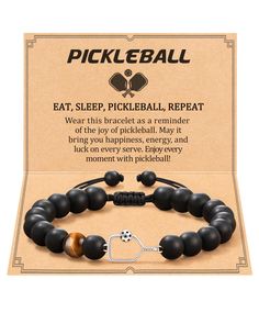 a black beaded bracelet with an orange and white ball charm on it, sitting in front of a cardboard box