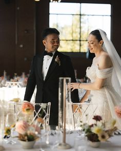 a bride and groom standing next to each other in front of a table with chairs