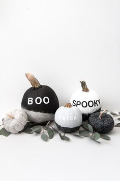 three black and white pumpkins with boo spelled on them sitting next to some leaves