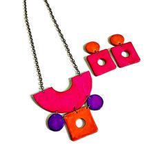 Make a bold fashion statement with this colorful jewelry set. Featuring a statement necklace with geometric shapes in eye-catching orange, pink, and purple hues, this set also includes large square earrings that can be worn as post or clip-ons. Each piece is crafted from hand-painted polymer clay for a unique touch. Measurements of jewelry pieces: Necklace- 3.25 inches high and 3.5 inches wide  Earrings- 2 inches long and 1.2 inch wide Sassy Sacha Jewelry is handmade with love in my workshop in Bold Multicolor Jewelry For Gifts, Modern Pink Jewelry For Party, Modern Pink Party Jewelry, Handmade Geometric Jewelry For Party, Bold Dangle Jewelry For Party, Vibrant Pink Jewelry For Party, Bold Orange Party Jewelry, Handmade Bold Jewelry For Party, Retro Handmade Pink Jewelry