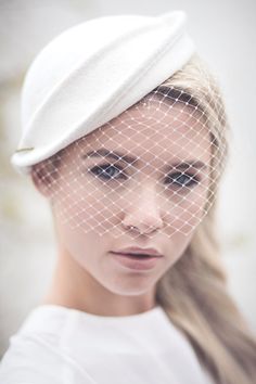 a woman wearing a white hat with a veil on it's head and looking at the camera