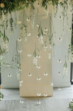 an arrangement of white flowers and greenery hanging from the ceiling in front of a wall