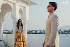 a man standing next to a woman in a yellow and white dress on top of a roof