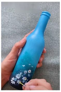 someone is painting the bottom of a blue bottle with flowers on it and holding a small toothbrush in their left hand