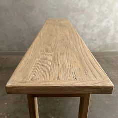 a wooden table sitting on top of a floor next to a gray wall and cement floor