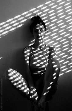 a woman sitting on top of a stool in front of a wall with sunlight streaming through it