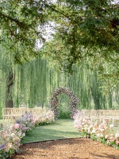 an outdoor ceremony setup with chairs and flowers in the foreground, surrounded by willow trees