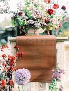 a sign that is sitting in front of some flowers on a fence with the name bar menu written on it