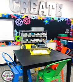 there is a black table with colorful chairs around it and a chalkboard on the wall