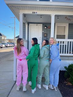 four women in matching outfits standing on the front porch of a house with their arms around each other