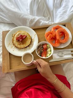 a person is eating breakfast in bed with fruit and pancakes on the tray next to them