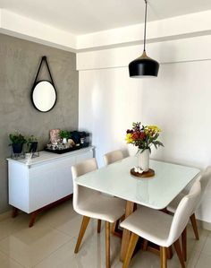 a dining room table with white chairs and flowers in a vase on the top of it