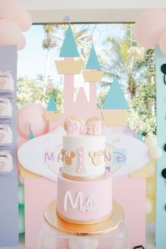 a pink and white cake sitting on top of a table next to some balloons in the air