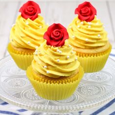 three cupcakes with yellow frosting and red roses on top sitting on a glass plate