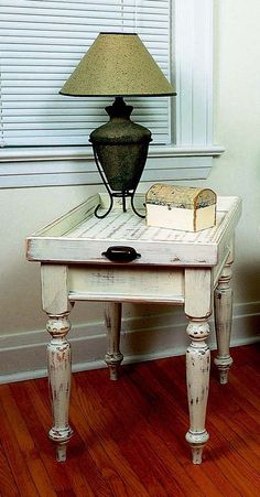 a table with a lamp and books on it in front of a window, next to a chair