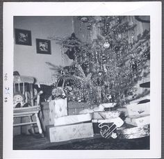 black and white photograph of a christmas tree with presents under it in a living room