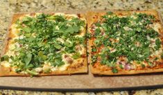 two square pizzas topped with greens on top of a counter