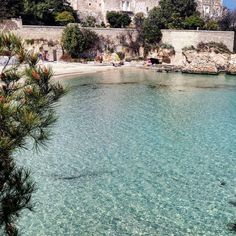 an old castle sits on top of a hill next to the ocean with clear blue water