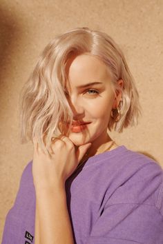 a woman with blonde hair wearing a purple shirt and gold hoop earrings is posing for the camera