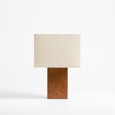 a lamp that is sitting on top of a wooden block with a white linen shade