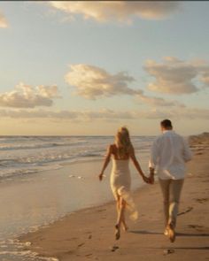 a man and woman walking on the beach holding hands