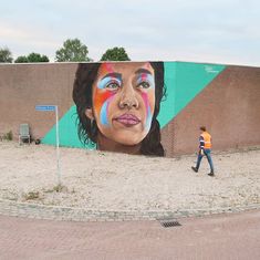 a man walking past a large mural of a woman's face on the side of a building