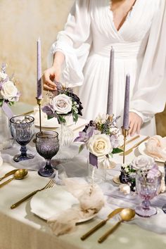 a woman in white dress standing next to a table with flowers and candles on it