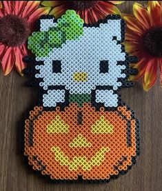 a cross stitch hello kitty sitting on top of a pumpkin with flowers in the background