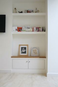 a white shelf with some pictures on it and a tv in the corner behind it