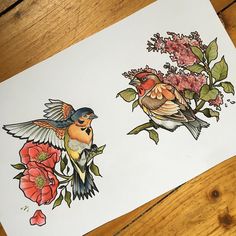 two birds sitting next to each other on top of a wooden table with flowers and leaves