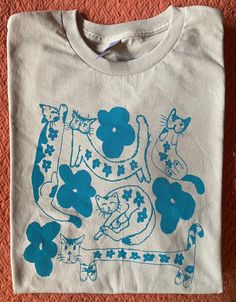 a t - shirt with an image of cats and flowers on it sitting on the floor