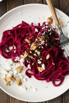 a white plate topped with red pasta and garnished with walnuts, fettuccine and parmesan cheese