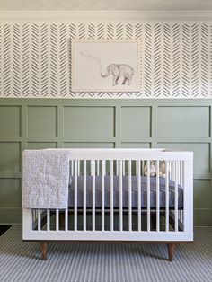 a white crib in front of a green wall with an elephant painting on it