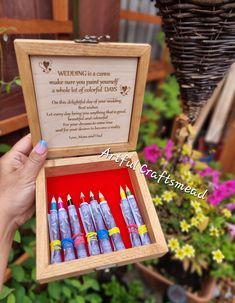 a person holding a wooden box filled with small crayons in front of flowers