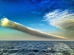 a very long cloud in the middle of the ocean with blue sky and white clouds