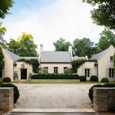 the entrance to a large white house surrounded by trees and bushes with hedges on either side