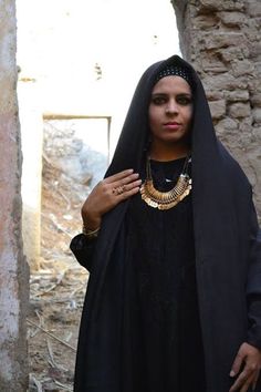 a woman wearing a black dress and gold necklace standing in front of an old building