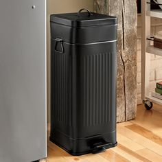 a black trash can sitting next to a metal freezer on a hard wood floor