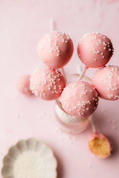 pink cake pops with white sprinkles in a glass jar next to a plate