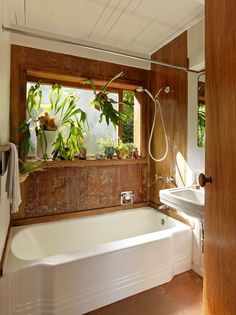 a bath tub sitting under a bathroom window next to a sink and a shower head